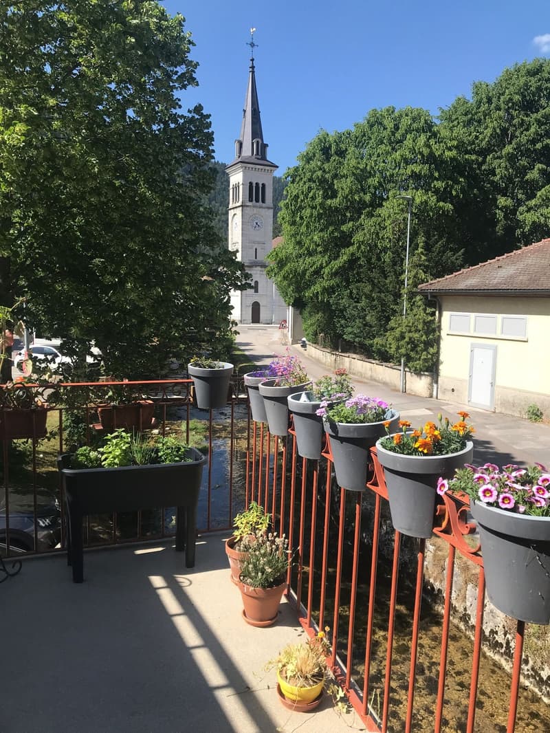 Terrace with plants, fenced with red metal railing, church building in the background