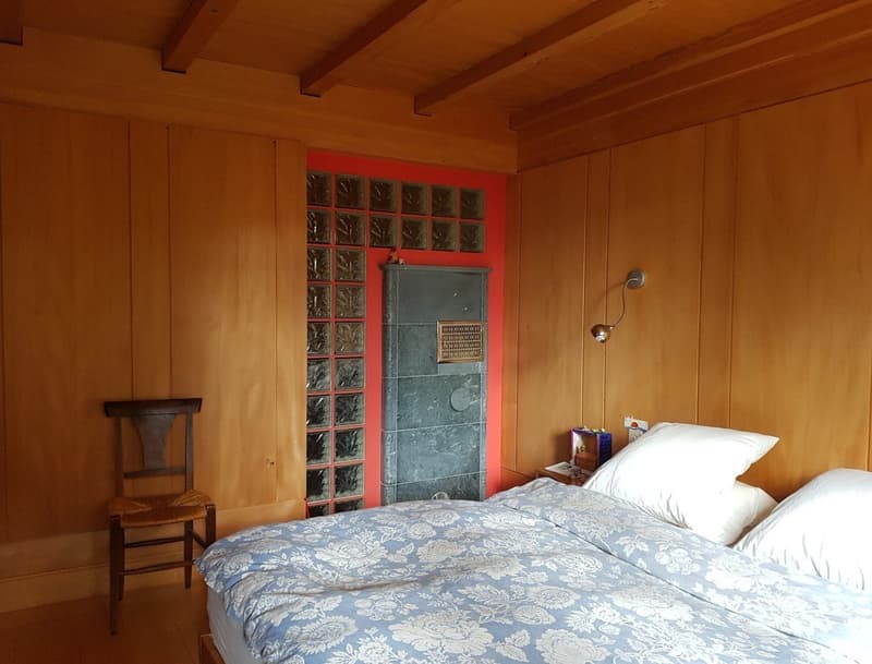 wooden walls, fireplace, wooden chair, blue bedspread with white flower print, bedside table