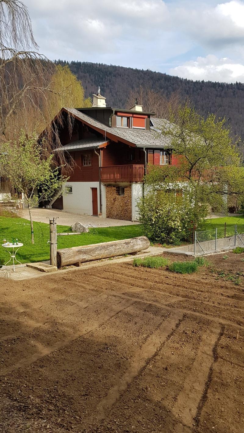 2 story house, red wooden exterior, large balcony, front garden with table and log