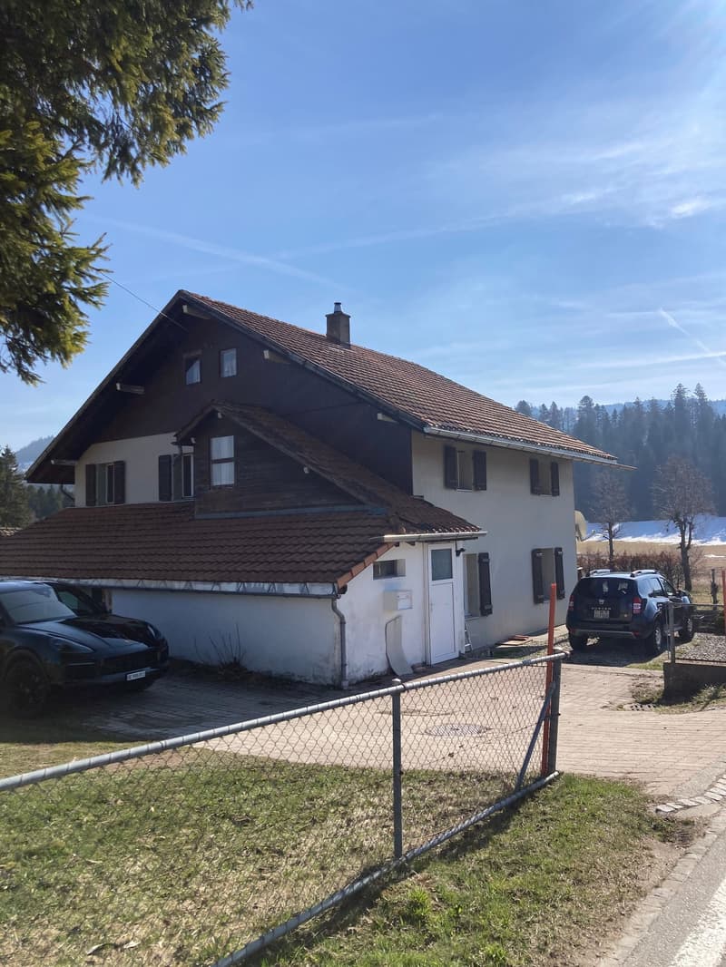 2 story house, brown roof, white walls, 2 cars parked in front, fence, trees, mountains in the background