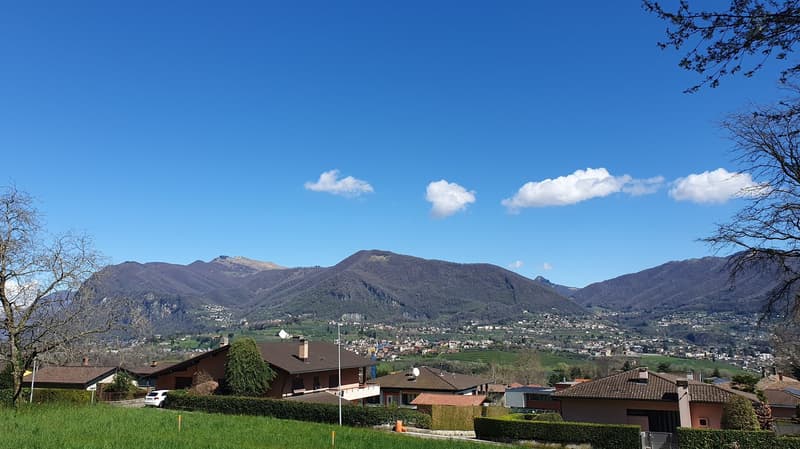 Rural landscape with houses, mountains, and town in the distance.