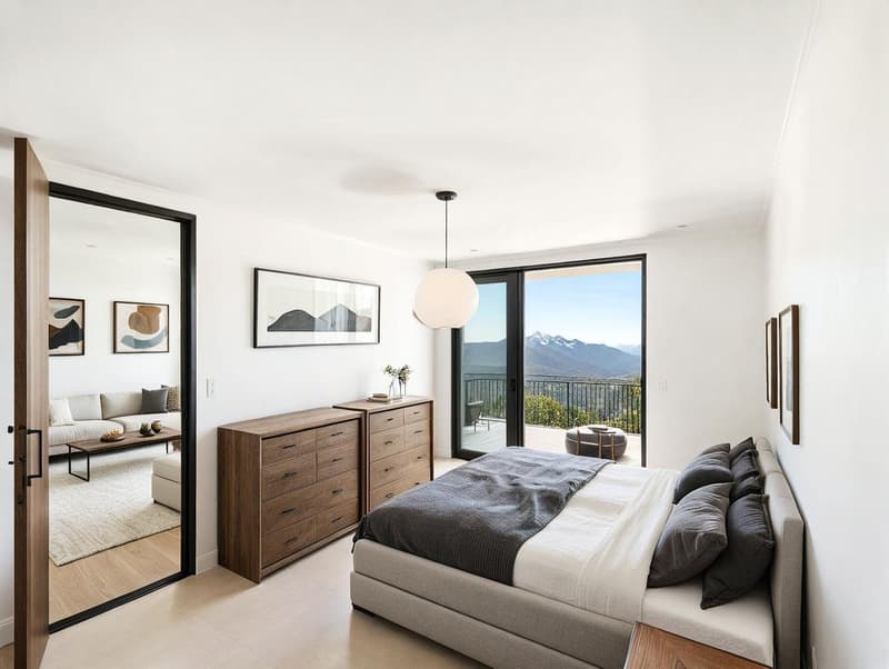 white walls, wooden floor, sliding glass door to balcony, bed with pillows, dresser, couch, coffee table, carpet, artwork, mountain view