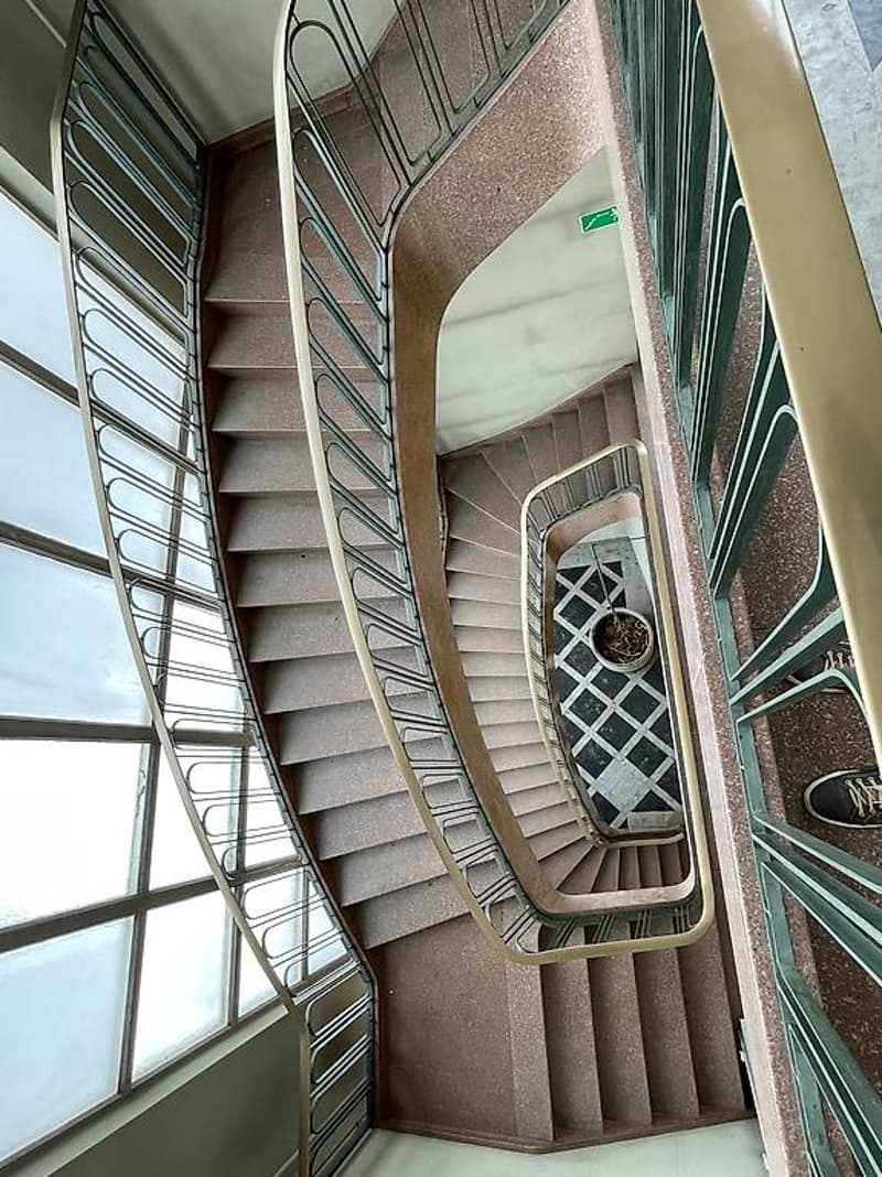 Double spiral staircase with brown steps and metal railings, windows on both sides
