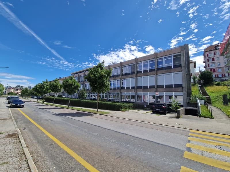 Multistory building, modern architecture, concrete exterior, numerous windows, parking area, streetlight, multiple parked cars