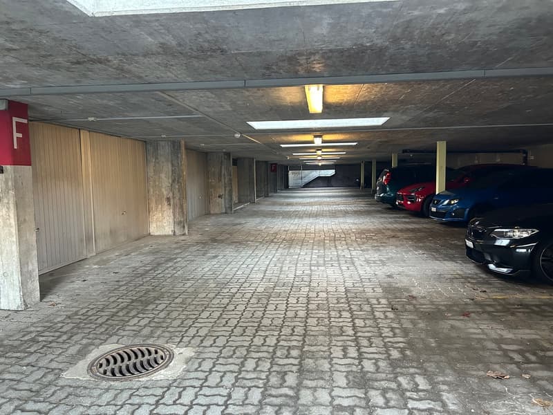 underground parking area, brick pavement, several parked cars, white and red signage