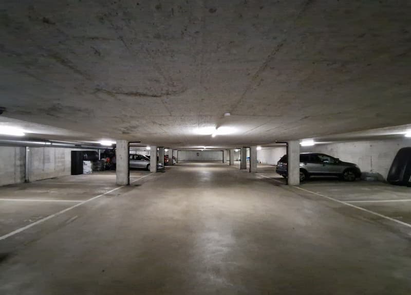 concrete floor, white ceiling, rows of parking spots, lights on the ceiling, metal columns, some cars parked