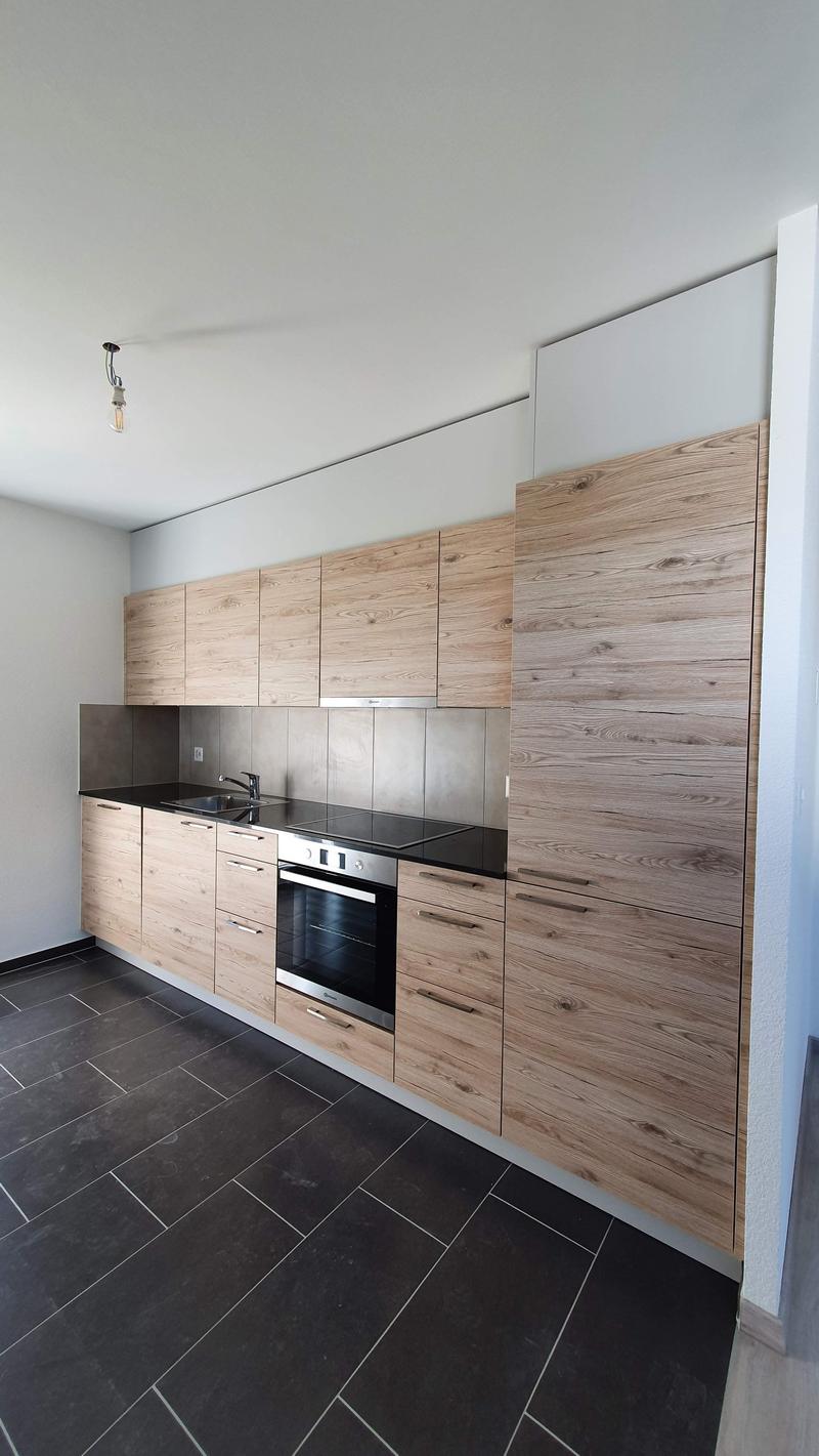 Modern and minimalistic kitchen with wooden cabinets, black countertops, built-in oven and sink with faucet, light fixtures