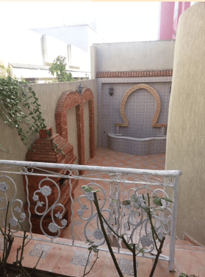 Courtyard area with a tile floor, decorative wall arches, outdoor grill, and decorative plants. The courtyard leads to an outdoor bathroom with a sink and a decorative wall.