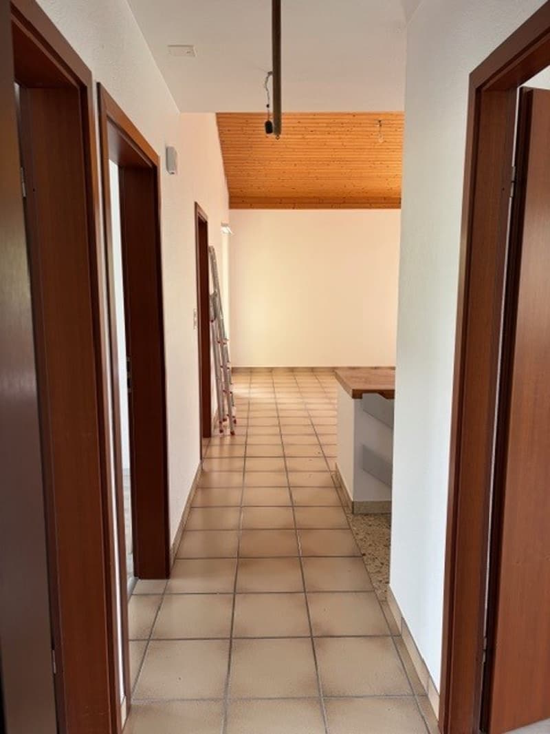 Empty hallway with tiled floor, wooden doors, wooden ceiling, and a ladder leaning against the wall.