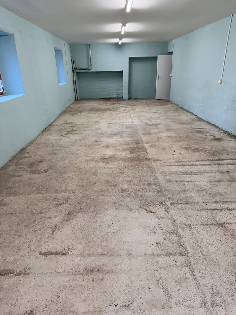 Empty room, concrete floor, concrete walls, three small windows, two doors, ceiling with three lights