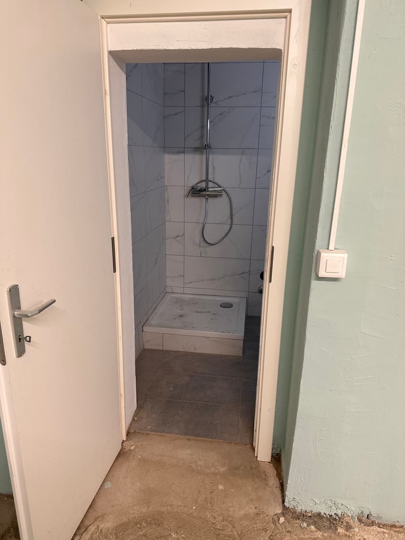 Small shower room with shower, tiled floor and walls, and a door opening to the left.