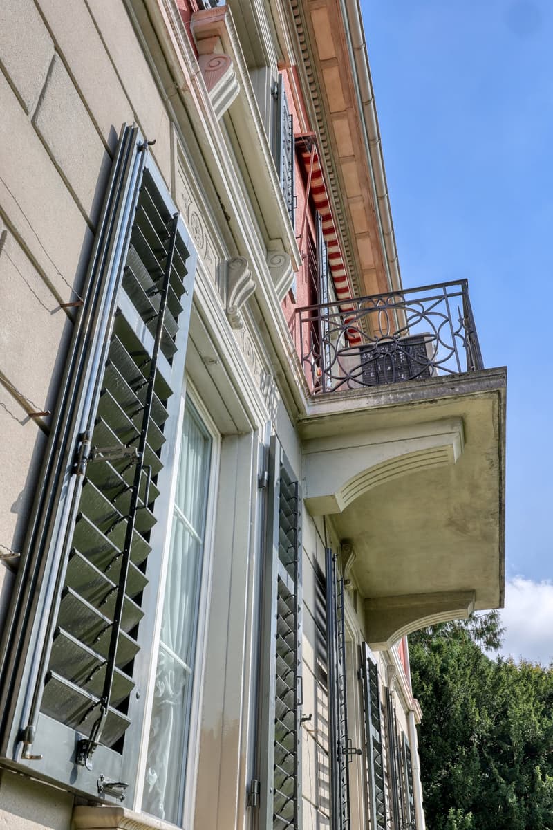 Facade with windows, balcony with wrought iron railing, shutters, red brick wall