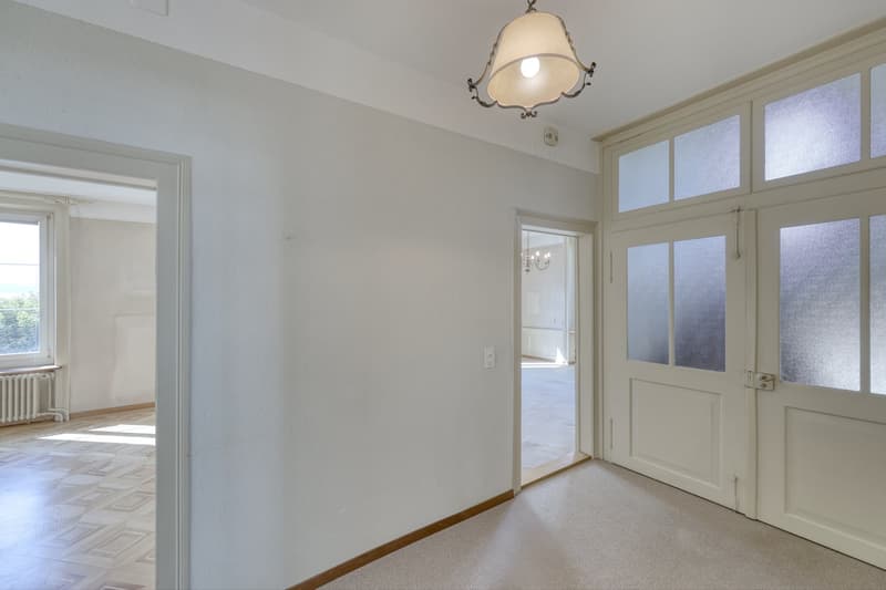 Empty room with white walls, wooden floor, white doors, radiator, chandelier, glass window