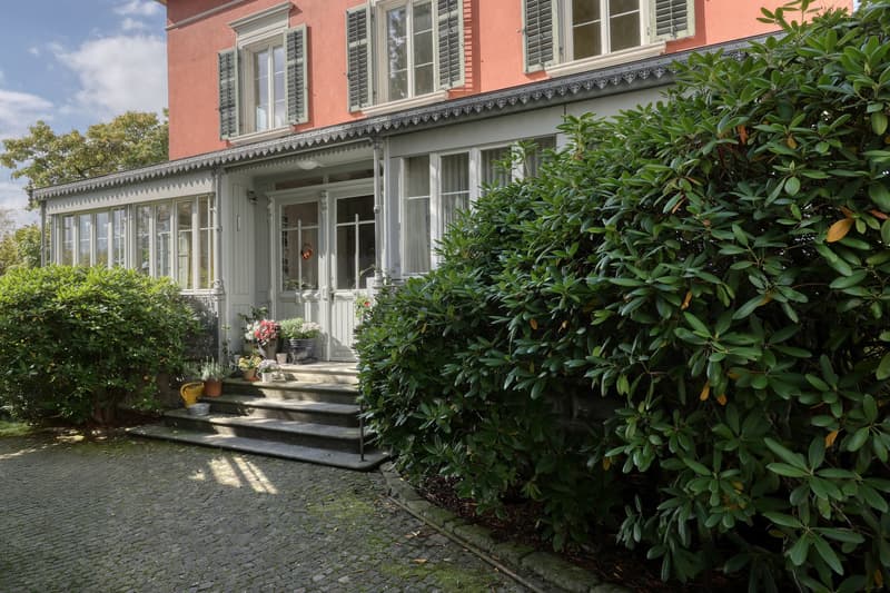 2 story house, red brick, white windows, steps leading to entrance, garden with shrubs and flowers