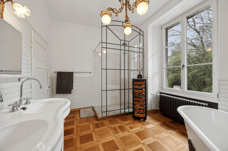 bathroom with a freestanding bathtub, white sink, glass shower, white tiles, wooden floor, radiator, windows