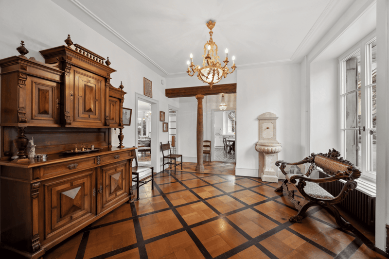 elaborate wooden furniture, hardwood floor with black trim, chandelier, wooden bench, radiator, windows