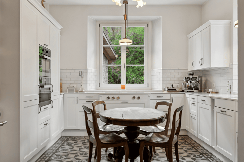 Modern kitchen with white cabinets, a round dining table, large window, tile flooring, modern appliances
