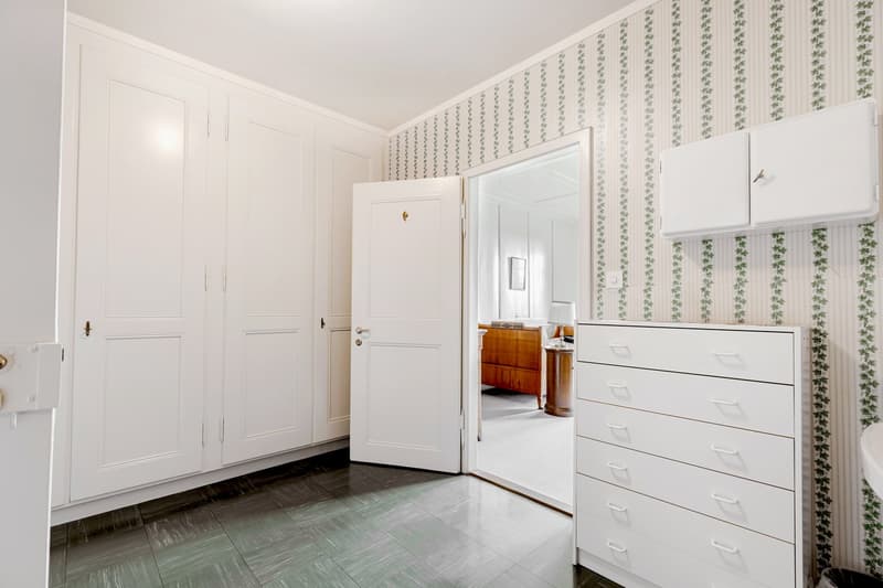 Large room, wardrobes, a tall drawer, open doors to another room with a bed and desk.