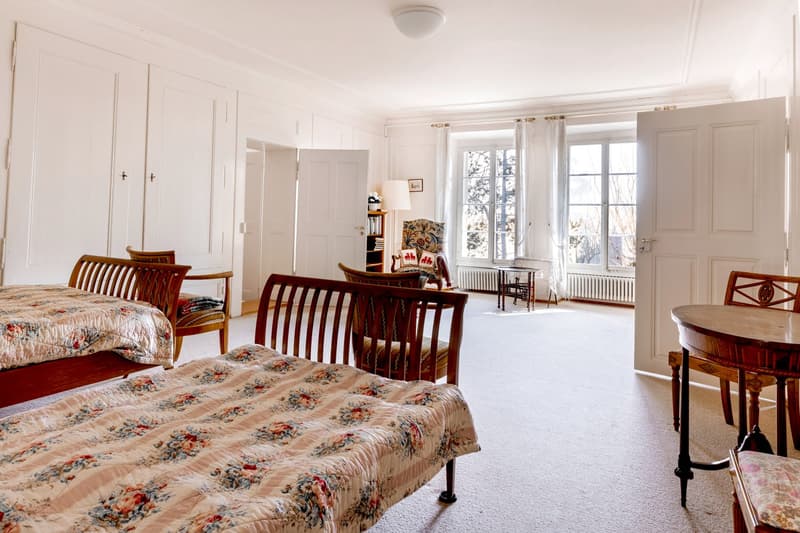 Two beds, wooden furniture, desk, lamp, radiator, white walls, window, door