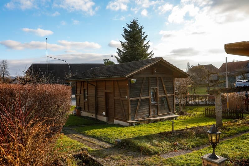 Raised ground floor wooden house with brown roof, small garden, front door with porch