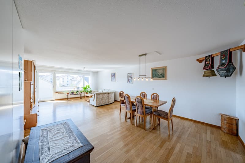Dining room with wooden floor, dining table, chairs, couch, and a window with a view