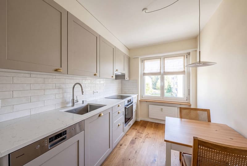 modern kitchen with white cabinets, wooden floor, white tiles, stainless steel sink, dishwasher, oven, window, radiator