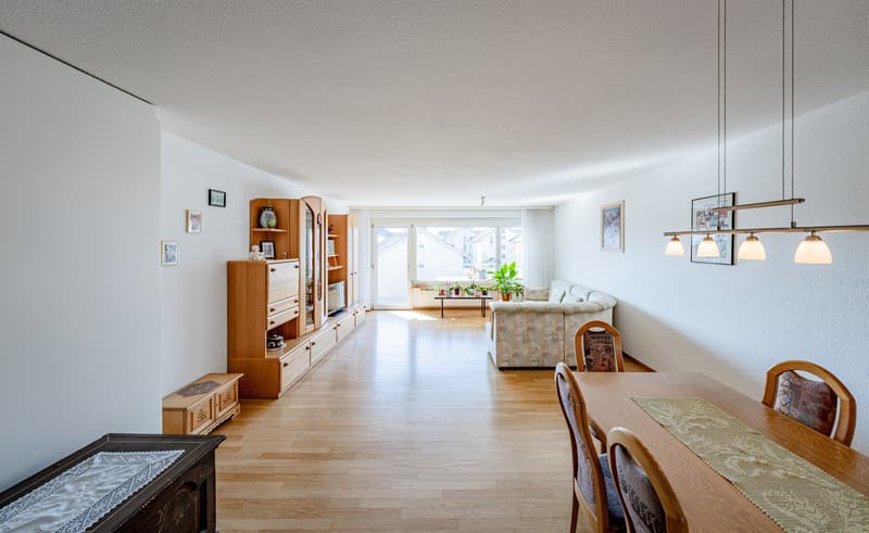 Dining room with wooden floor, dining table, chairs, wooden cabinet, TV stand, couch, window, plants, picture frames, chandelier