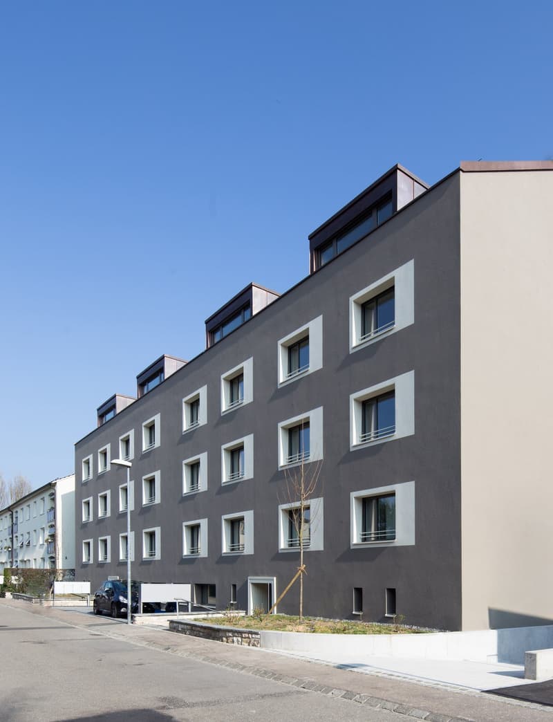 multi-story residential building, gray exterior, multiple windows, car parked in front