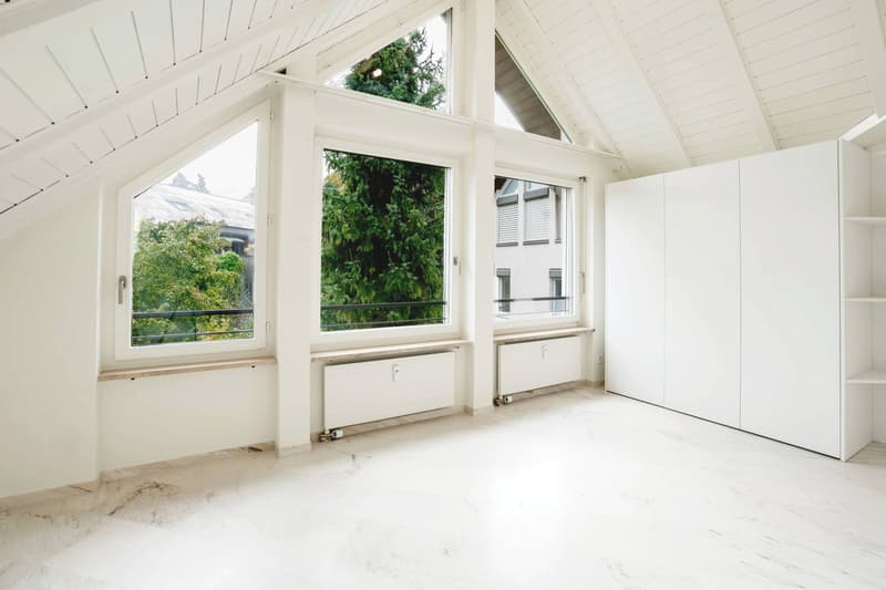Large triangular windows, balcony, wooden white flooring, white painted walls, built-in storage, white wardrobe, no furniture