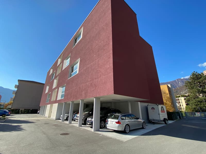 Red building with many windows, multiple cars parked inside the garage, car trailer on the side