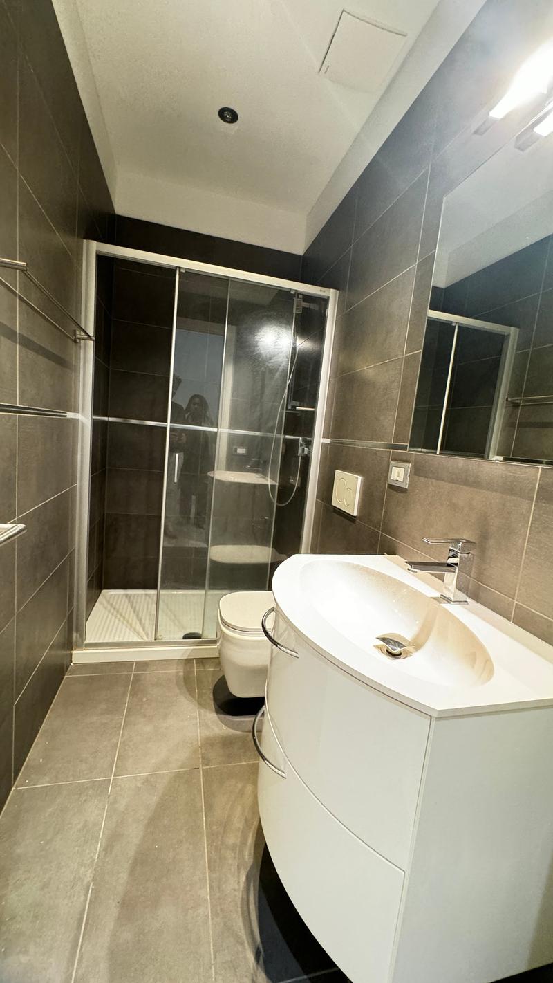 Bathroom with glass door, white sink, white toilet, and silver fixtures.