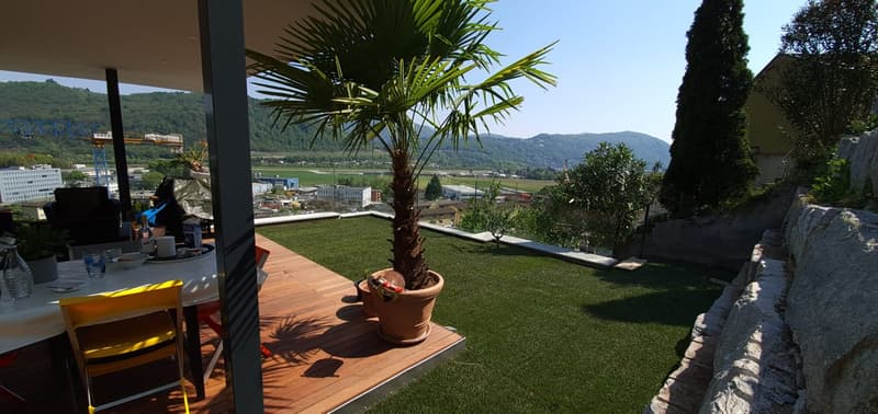 Terrace with wooden floor, artificial grass, palm tree, table, chairs, view of the mountains