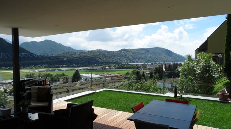 Outdoor dining area with a table and chairs, a grassy area, and a view of the mountains and city.