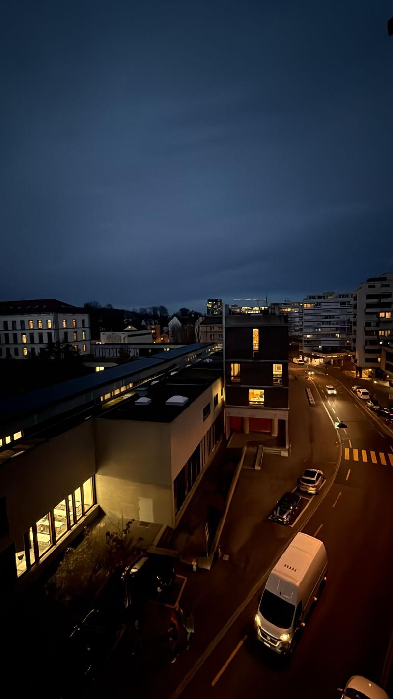 Aerial view of a building, modern architectural style, multiple windows, parking area on the street, cars driving on the road.