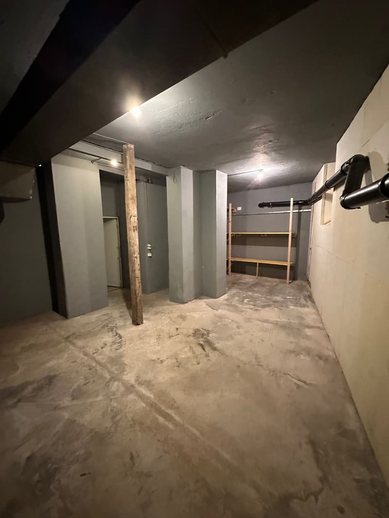 A storage room with concrete floors, walls painted in gray, an entrance, and a wooden pillar