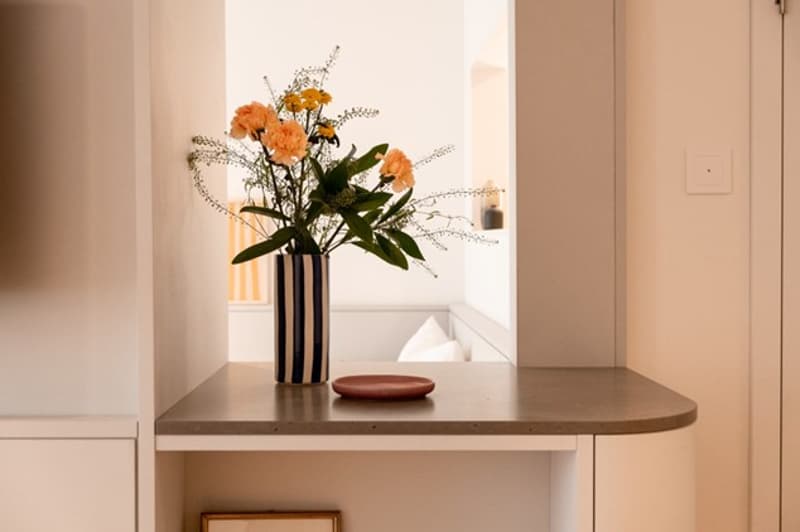 A room with a table featuring a vase with flowers, a decorative plate and picture frame underneath.