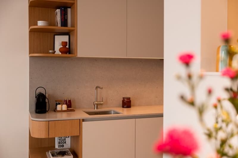 Modern kitchen with wooden cabinets, concrete countertop, sink with faucet, shelves with books and decorative items, flowers on the right side
