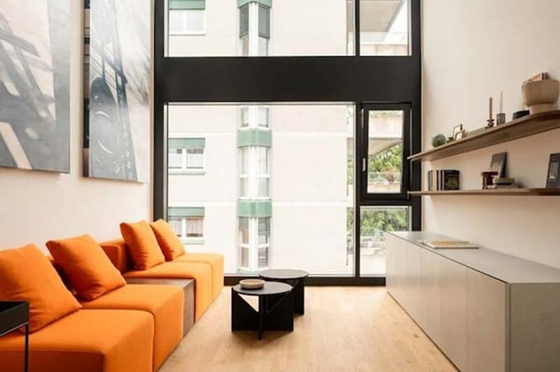 modern living room, large orange couch, wooden floors, large glass window, black coffee tables, white walls