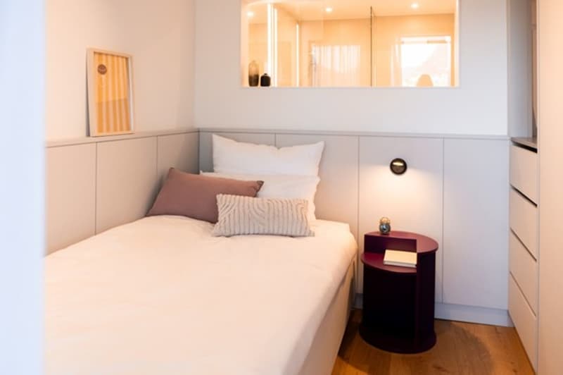 single bed, nightstand, pillow, side mirror, wooden floor, wall mounted light