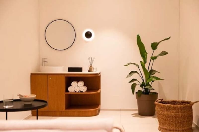 Small bathroom with sink, mirror, wooden shelf, towels, potted plant, small black table