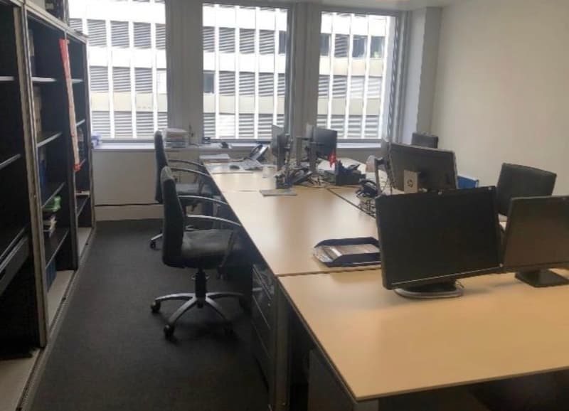 empty office, several desks with computers, chairs, shelves, and a window with blinds