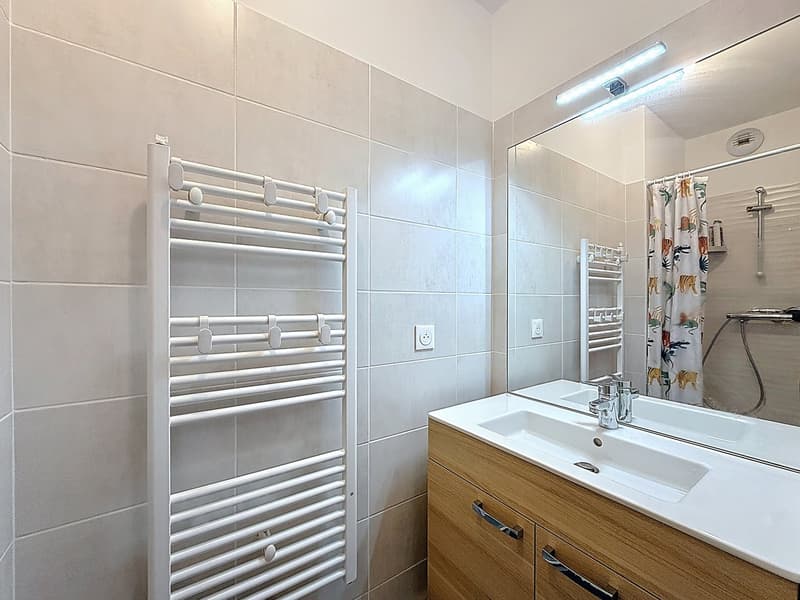 white tiled walls, white sink, wooden cabinet, white towel rack, mirror, shower curtain