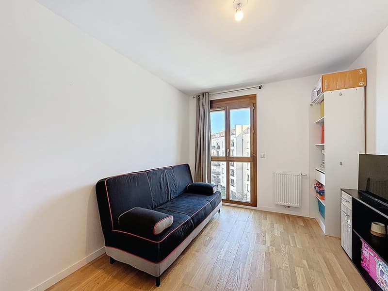 A room with a couch, wooden floor, white walls, a window, and a radiator.