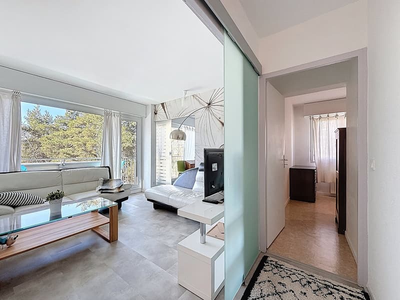 modern living room with white couch, glass coffee table, white TV stand, white walls, large windows, balcony