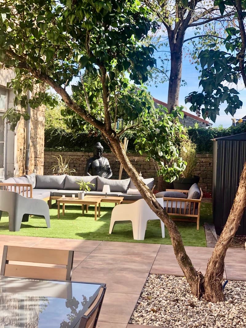 Outdoor seating area with a couch, chairs, and tables, a Buddha statue, and a tree.