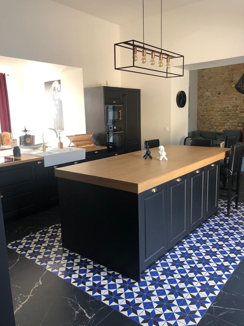 modern kitchen with island, black cabinets, wooden countertop, blue and white tiles, chandelier, black marble flooring