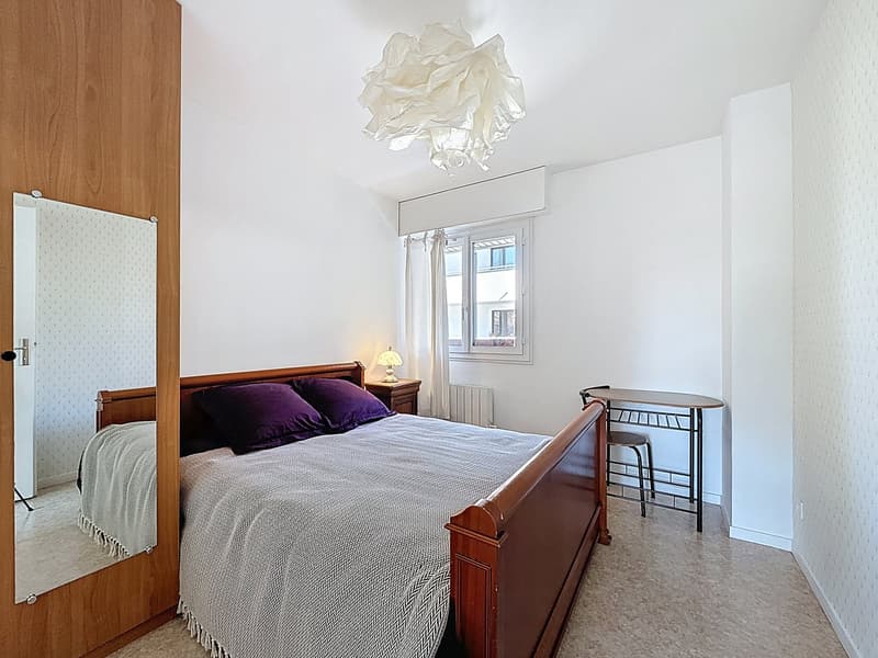 Bedroom with a bed, nightstand, lamp, mirror, table, chair, and window with curtains