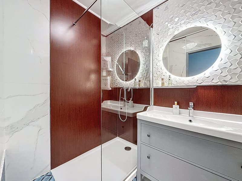 modern bathroom with white marble tiles, glass shower enclosure, double sink, wooden wall paneling, round mirrors, and a shower head