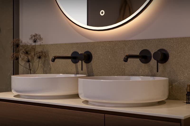 two white sinks with modern faucets, round mirror, brown countertop, illuminated mirror