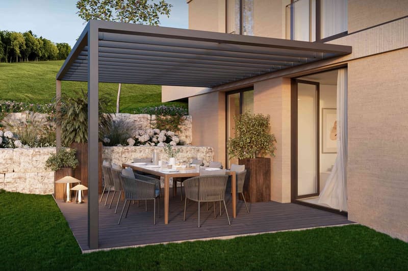 Outdoor dining area with a wooden table and chairs, covered by a metal pergola, and a stone wall with greenery in the background.